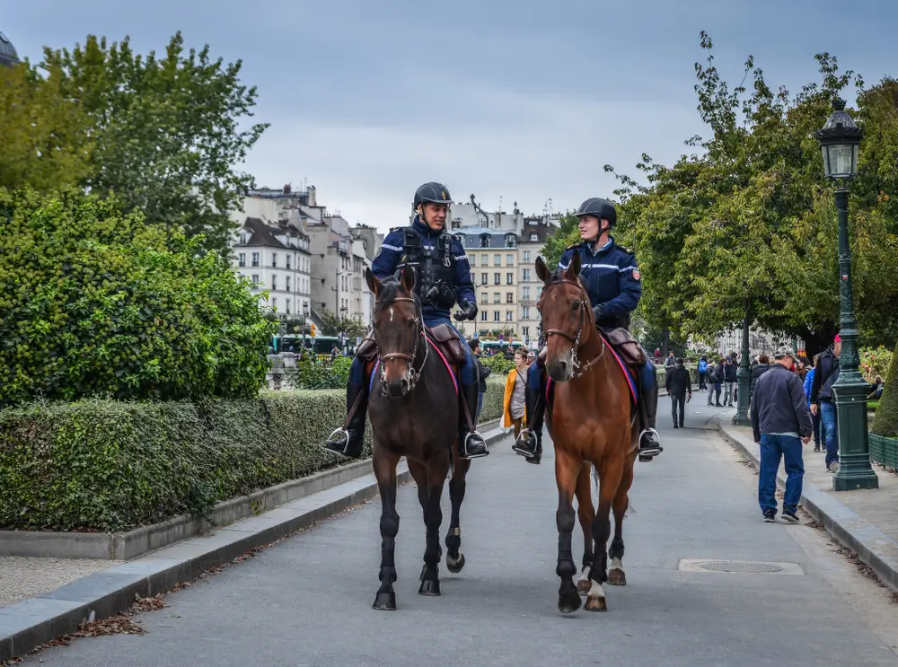 Deux gendarmes à cheval patrouillent dans une rue urbaine française avec des bâtiments haussmanniens en arrière-plan