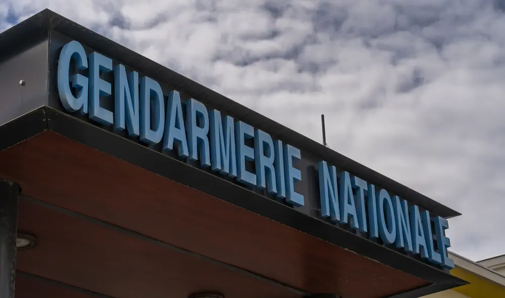 Enseigne Gendarmerie Nationale sur bâtiment de caserne avec famille et enfants dans cour intérieure en arrière-plan