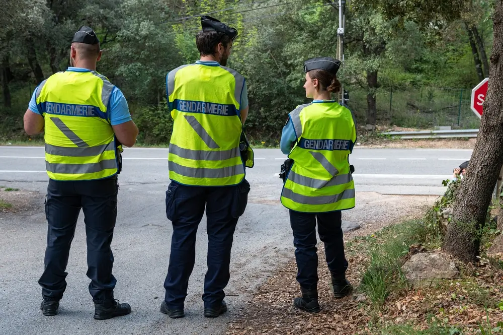 Trois gendarmes en gilets haute visibilité jaunes surveillant une route dans un environnement boisé lors d'un contrôle routier