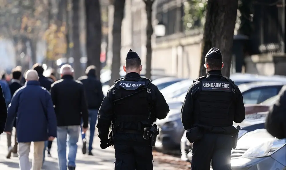 Deux gendarmes français patrouillent dans une rue urbaine avec des civils et des voitures en arrière-plan