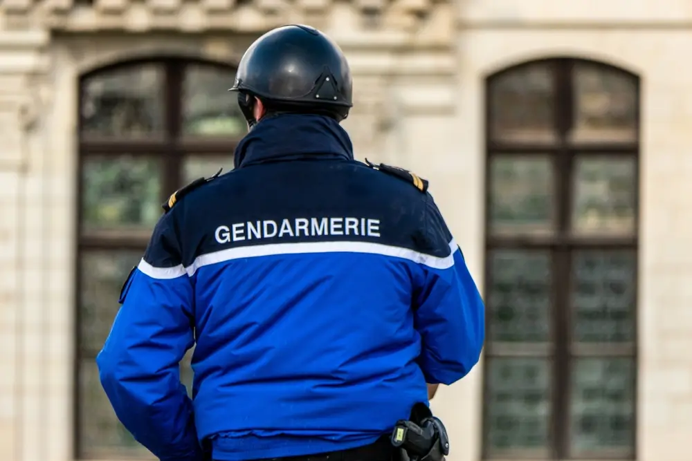 Gendarme en uniforme bleu avec casque et inscription "GENDARMERIE" de dos devant un bâtiment officiel