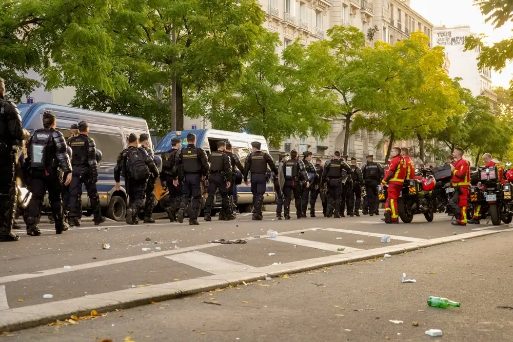 Police en formation dans une rue urbaine avec véhicules d'intervention et personnel médical en arrière-plan