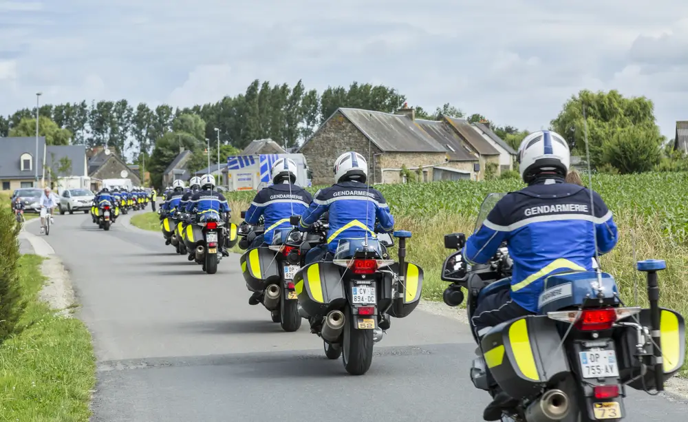 Escadron de motards de la gendarmerie en formation sur route de campagne française avec uniformes bleus réglementaires