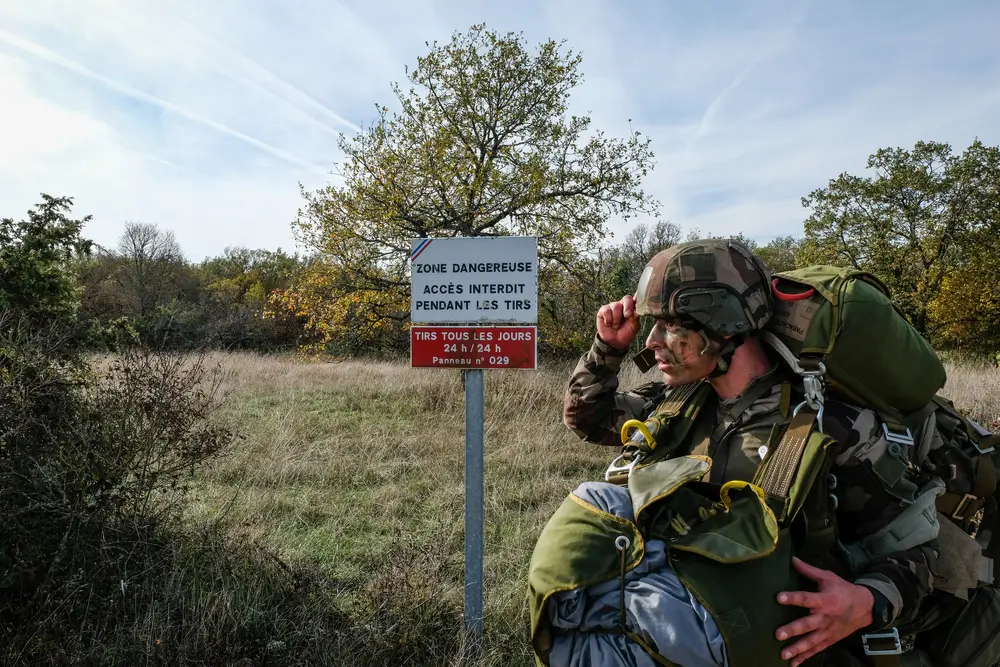 Militaire en tenue de combat portant un équipement lourd lors d'épreuves physiques de sélection en extérieur.