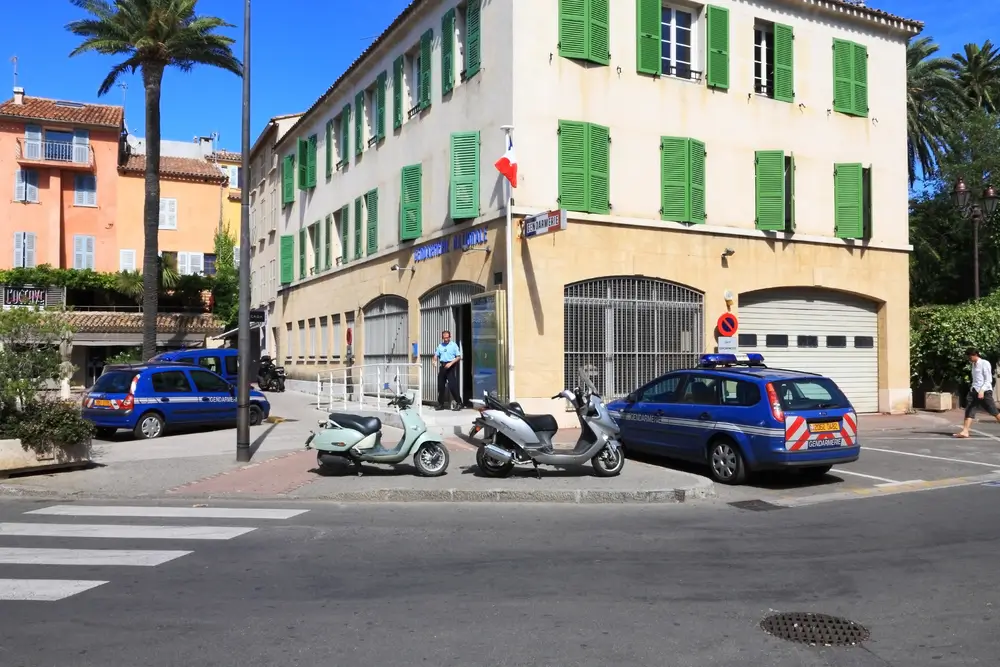 Bâtiment d'une brigade de gendarmerie avec des véhicules de service bleus stationnés devant la façade aux volets verts.