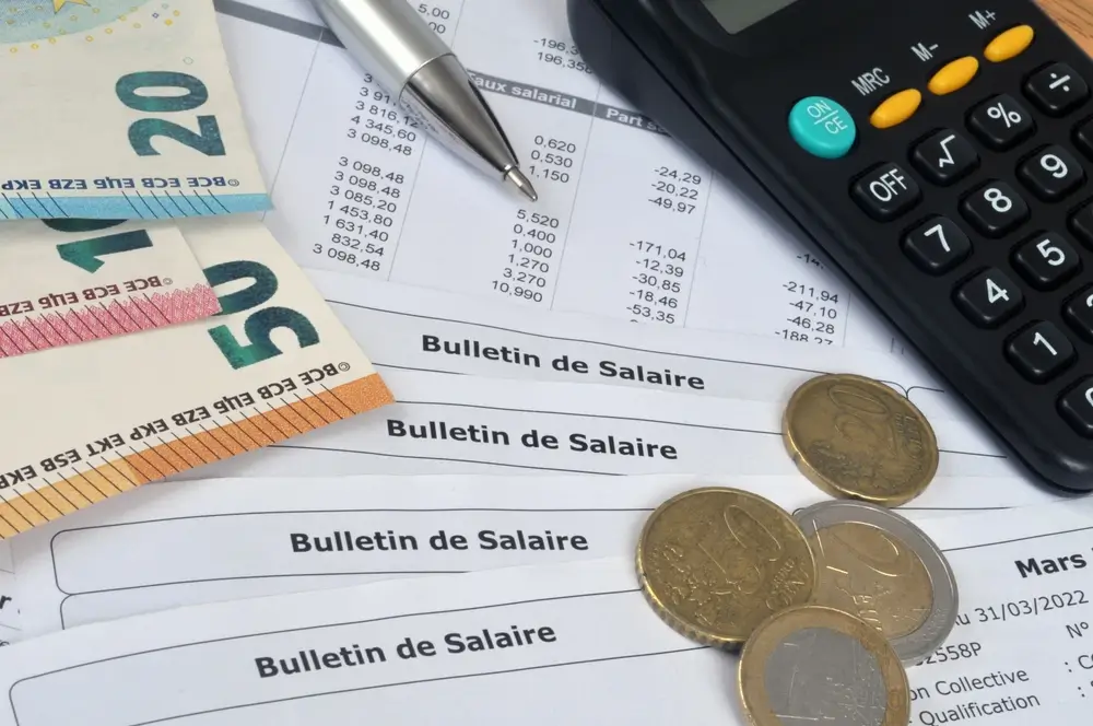 Bulletins de salaire, billets d'euros et calculatrice illustrant le calcul de la rémunération d'un fonctionnaire.