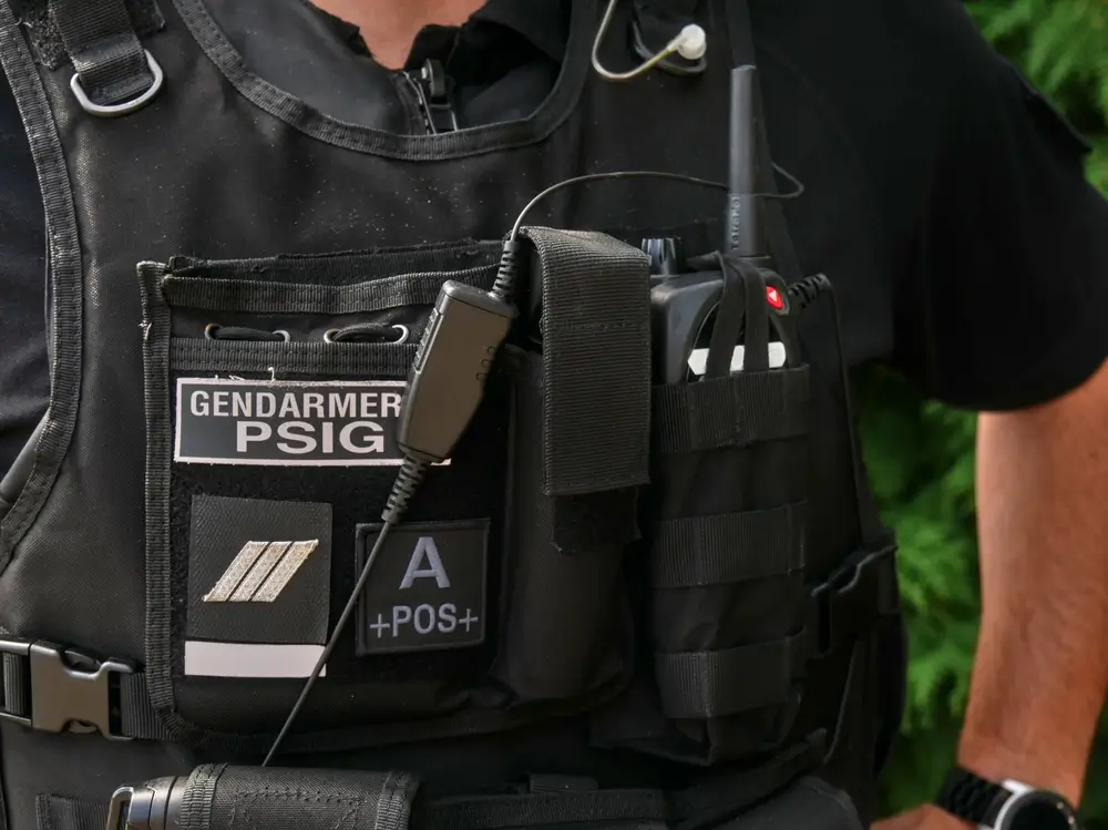 Gilet tactique de gendarmerie avec écusson PSIG et radio, porté par un gendarme en tenue d'intervention.