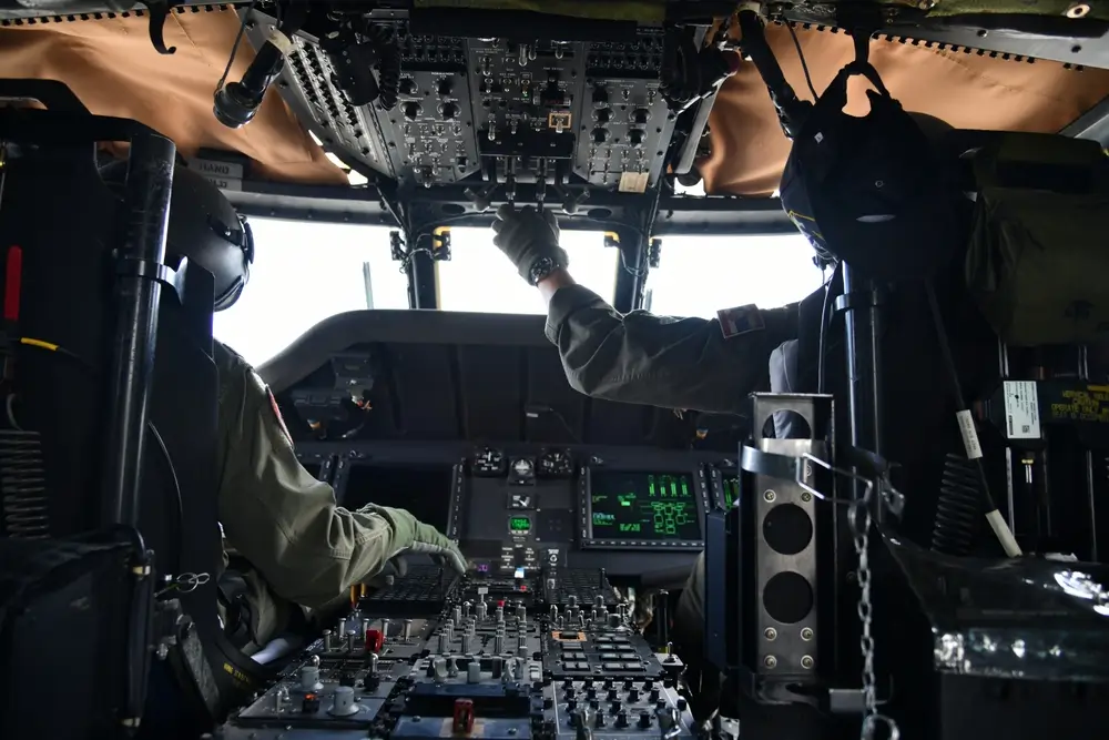 Pilote d'hélicoptère militaire en tenue de vol manipulant les instruments du cockpit lors d'une mission aérienne.