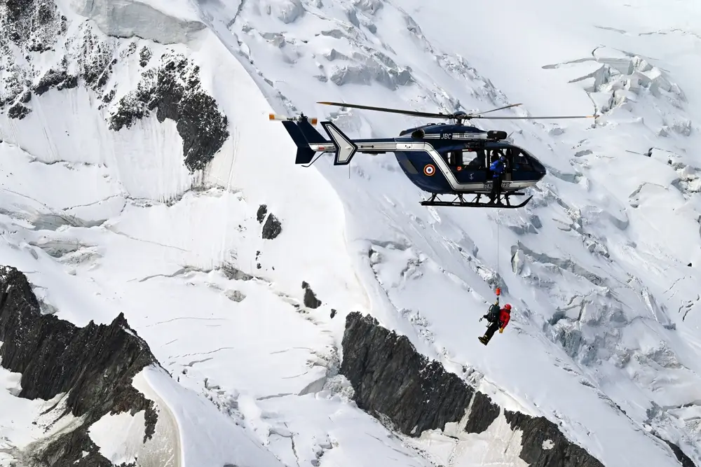 Hélicoptère de la gendarmerie réalisant un treuillage de secours en haute montagne avec le mécanicien de bord.