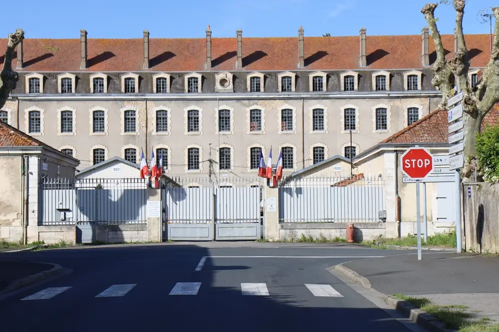 Caserne de gendarmerie et base militaire en zone rurale avec bâtiment en pierre, drapeaux français et entrée sécurisée.