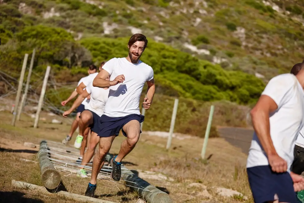 Recrues militaires courant sur un parcours d'obstacles lors d'épreuves physiques de formation en extérieur.