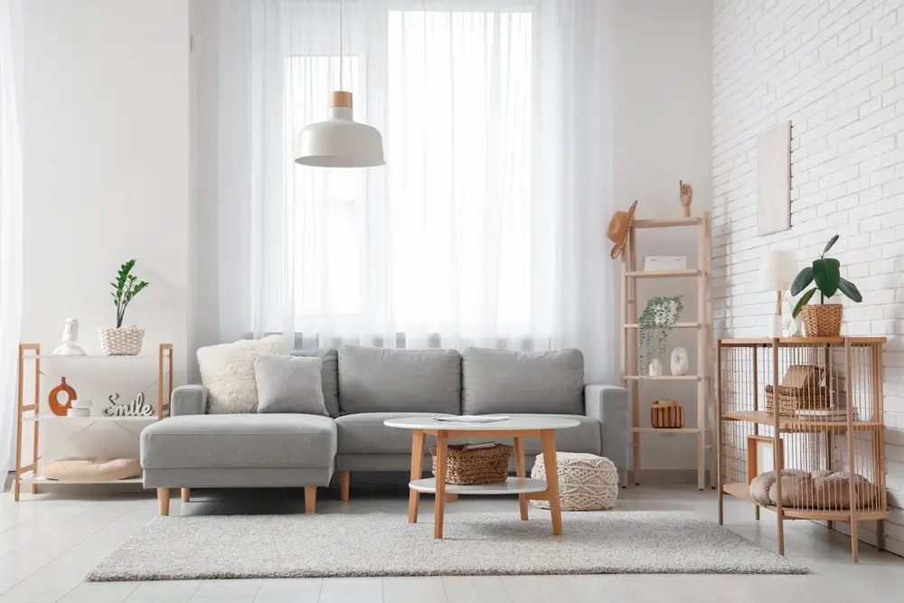 Salon meublé d'un appartement moderne avec canapé gris, mobilier en bois et grande fenêtre lumineuse.