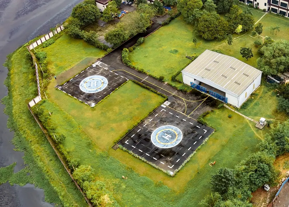 Vue aérienne de deux hélisurfaces et d'un hangar pour hélicoptères sur une base aérienne entourée de verdure.