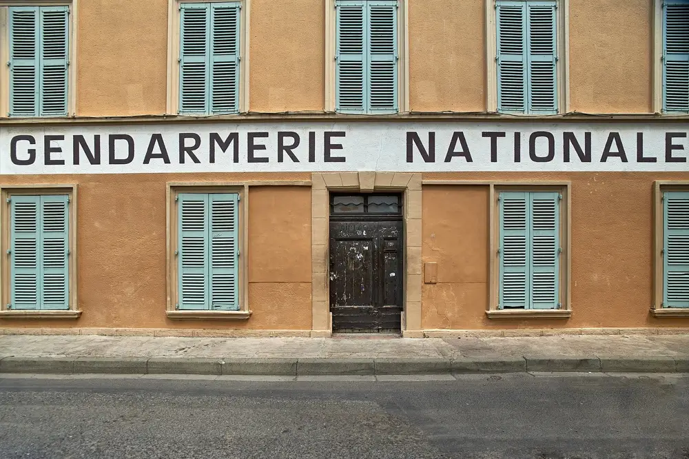 Façade ocre d'une brigade de gendarmerie nationale avec volets bleus dans une commune rurale.