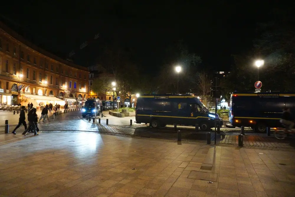 Plusieurs fourgons de gendarmerie en mission nocturne dans une rue animée, illustrant les sujétions du métier.
