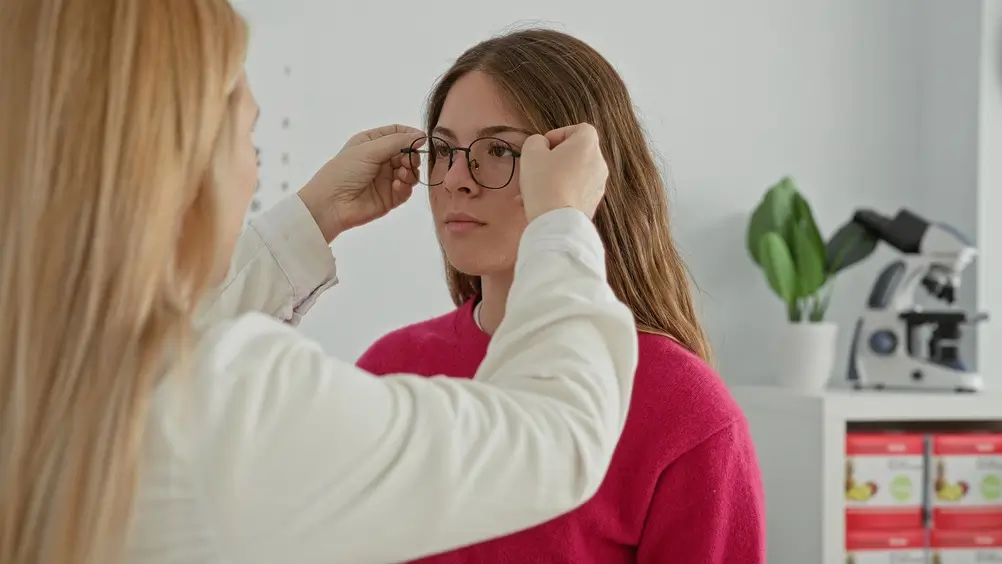 Une opticienne ajuste des lunettes sur une cliente lors d'un examen pour évaluer ses besoins de santé visuelle.