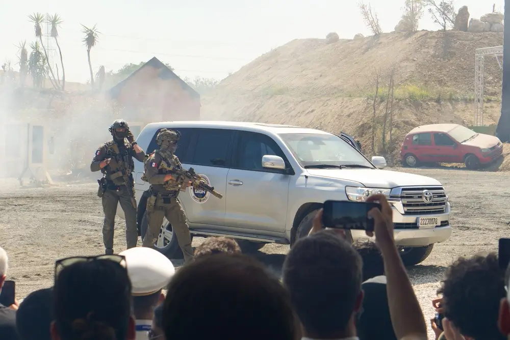 Gendarmes d'une unité d'intervention armée progressant avec des fusils d'assaut à côté d'un véhicule tactique blanc.