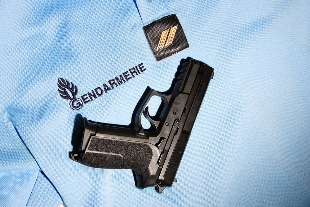 Galons dorés à chevrons de grade de la gendarmerie nationale posés sur un polo d'uniforme avec une arme de service.