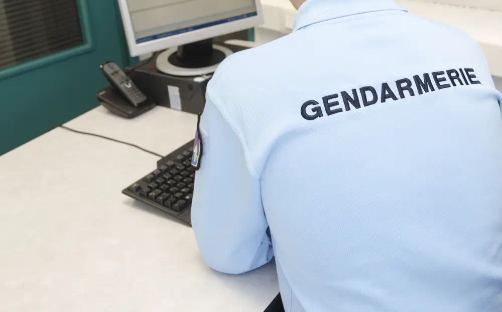Gendarme de dos à son bureau lors d'une réunion de briefing d'équipe au sein d'une brigade territoriale.