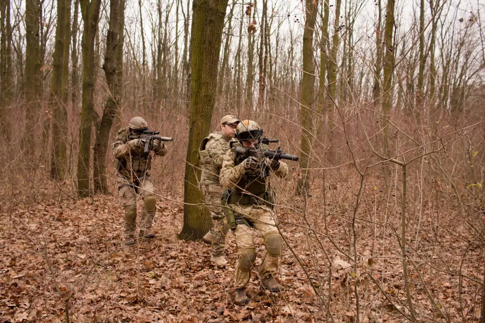 Recrues de la gendarmerie en formation militaire tactique, progressant avec armes et équipement en milieu forestier.
