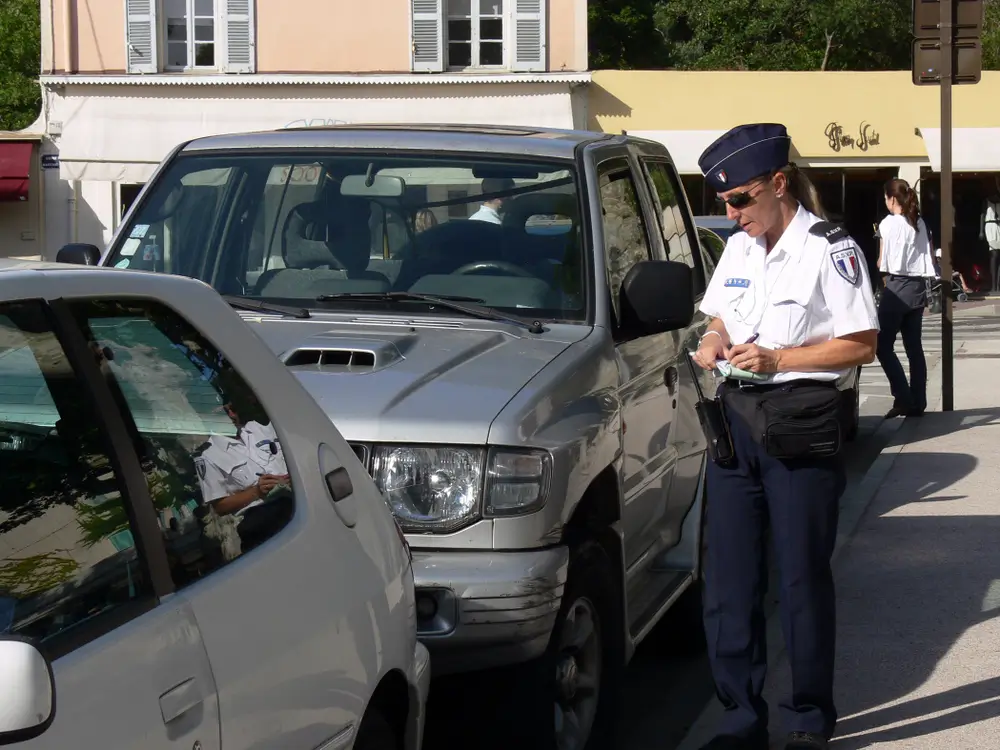 Une femme gendarme en uniforme effectue un contrôle routier et prend des notes à côté d'un véhicule arrêté.