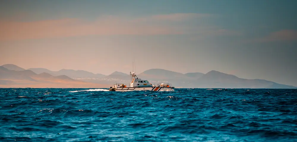 Vedette côtière de surveillance maritime naviguant le long d’un littoral montagneux.