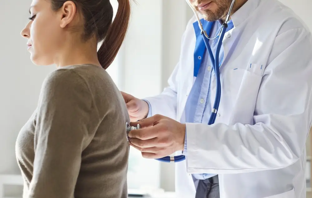 Médecin auscultant une patiente au stéthoscope lors d'une visite d'aptitude dans un cabinet médical.