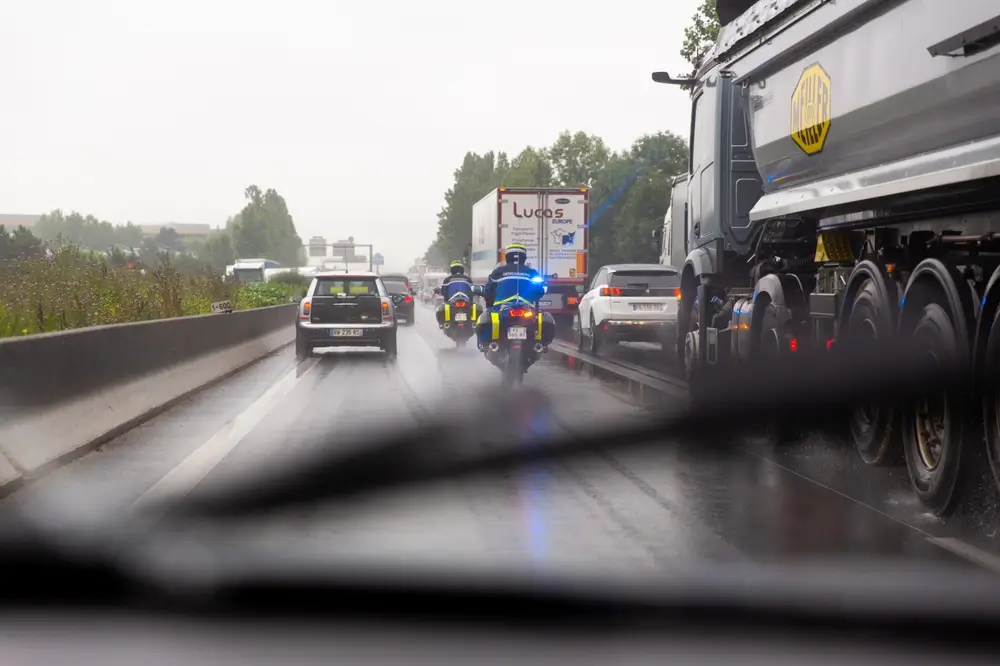 Deux gendarmes motocyclistes circulant sur une autoroute mouillée par la pluie au milieu d'un trafic dense.