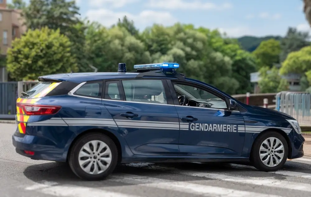 Véhicule de patrouille de la gendarmerie nationale en mission dans une rue, gyrophares bleus activés.