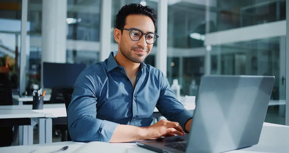 Un homme souriant remplit un formulaire d'adhésion en ligne sur son ordinateur portable dans un bureau.