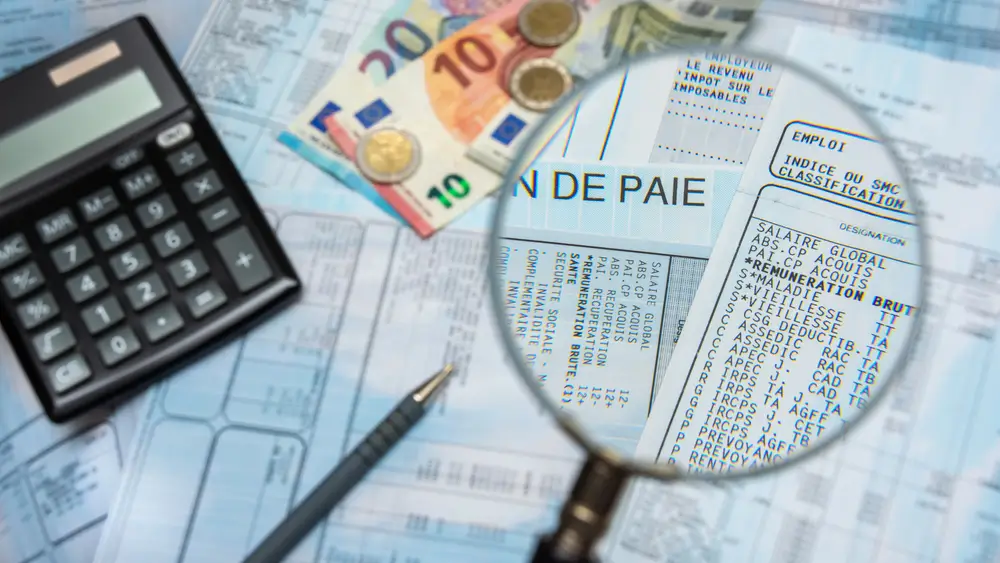 Loupe sur le détail d'une fiche de paie avec calculatrice et billets d'euros pour le calcul de la solde mensuelle.