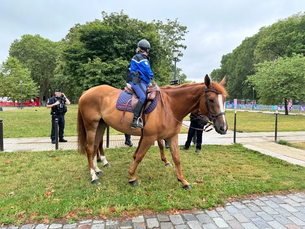 Cavalière de la Garde républicaine en uniforme sur son cheval alezan lors d’une patrouille dans un parc verdoyant.